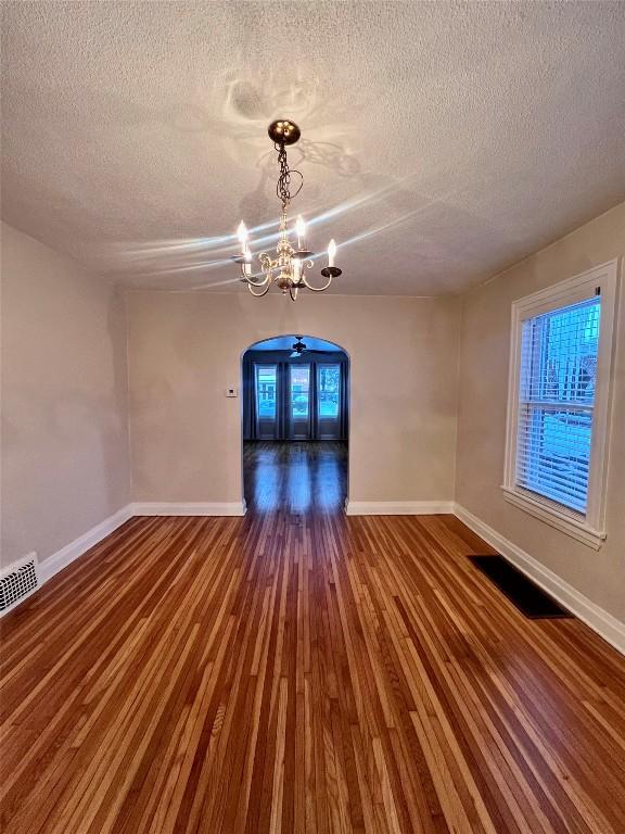 empty room with french doors, dark hardwood / wood-style flooring, a textured ceiling, and a notable chandelier