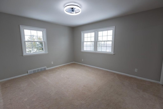 unfurnished room featuring baseboards, visible vents, a wealth of natural light, and light colored carpet