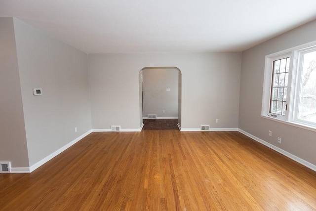 spare room featuring arched walkways, visible vents, baseboards, and wood finished floors