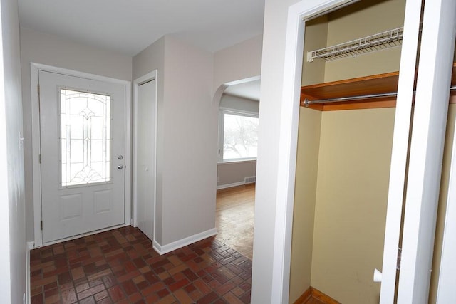 foyer with brick floor, baseboards, visible vents, and arched walkways