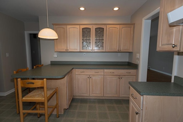 kitchen with dark countertops, light brown cabinets, glass insert cabinets, and decorative light fixtures