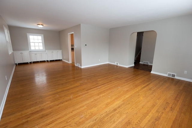 unfurnished room featuring light wood-style floors, visible vents, and arched walkways