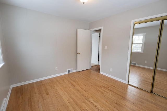 unfurnished bedroom with light wood finished floors, visible vents, and a closet