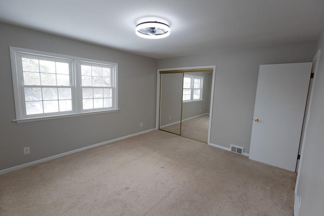 unfurnished bedroom featuring light carpet, baseboards, visible vents, and a closet