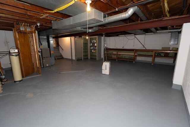 unfinished basement with electric panel, heating unit, and stairs