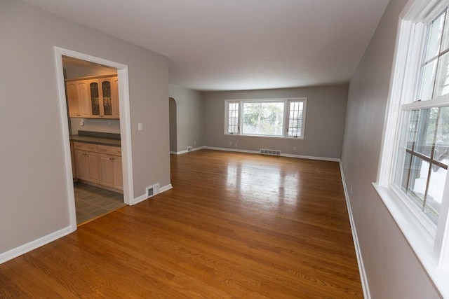 unfurnished room featuring arched walkways, visible vents, baseboards, and wood finished floors