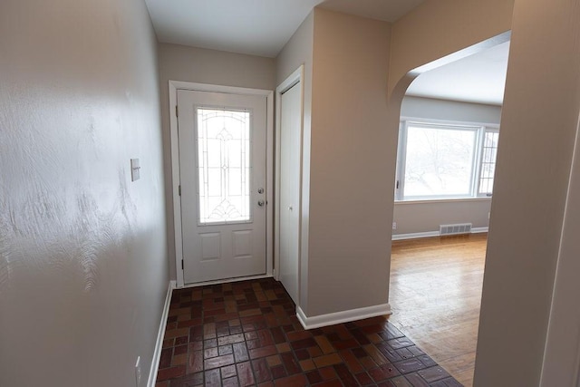 doorway to outside with a wealth of natural light, brick floor, visible vents, and baseboards