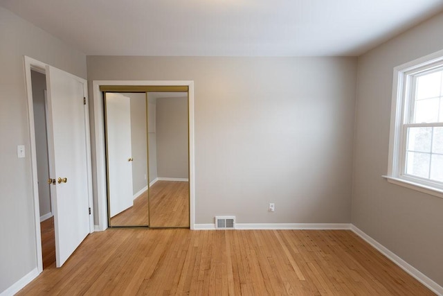 unfurnished bedroom featuring light wood-style flooring, a closet, visible vents, and baseboards