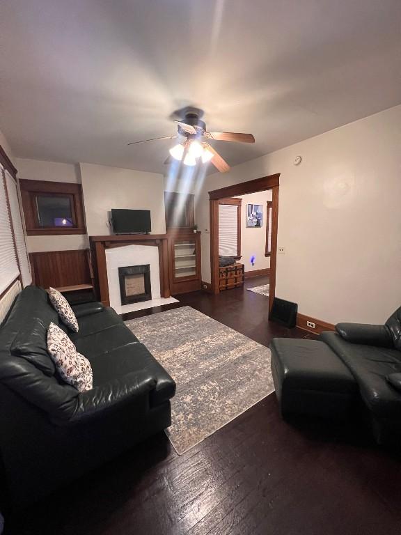 living room featuring a fireplace with flush hearth, dark wood-style flooring, ceiling fan, and baseboards