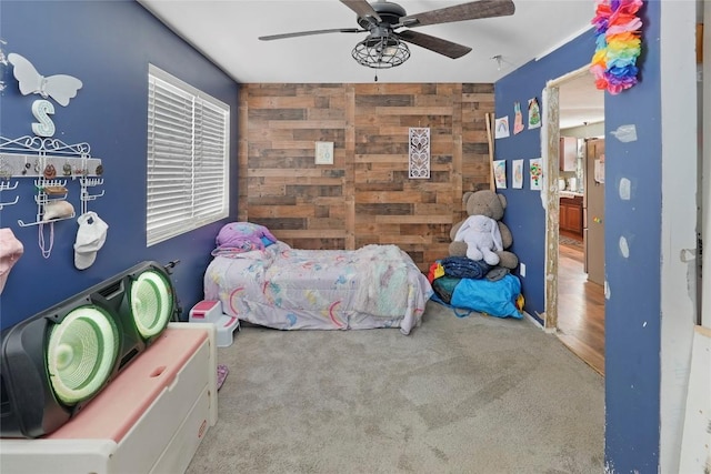 carpeted bedroom featuring ceiling fan and wood walls