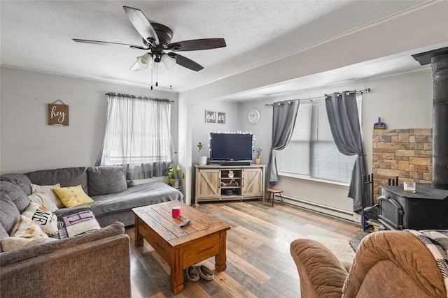 living room featuring a textured ceiling, a wood stove, a baseboard radiator, hardwood / wood-style flooring, and ceiling fan