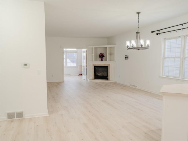 unfurnished living room featuring a tile fireplace, a chandelier, and light wood-type flooring