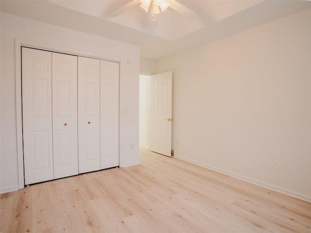 unfurnished bedroom with ceiling fan, a closet, a tray ceiling, and light hardwood / wood-style flooring