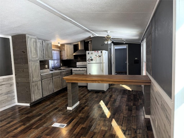 kitchen featuring lofted ceiling, sink, dark hardwood / wood-style floors, white appliances, and wall chimney range hood