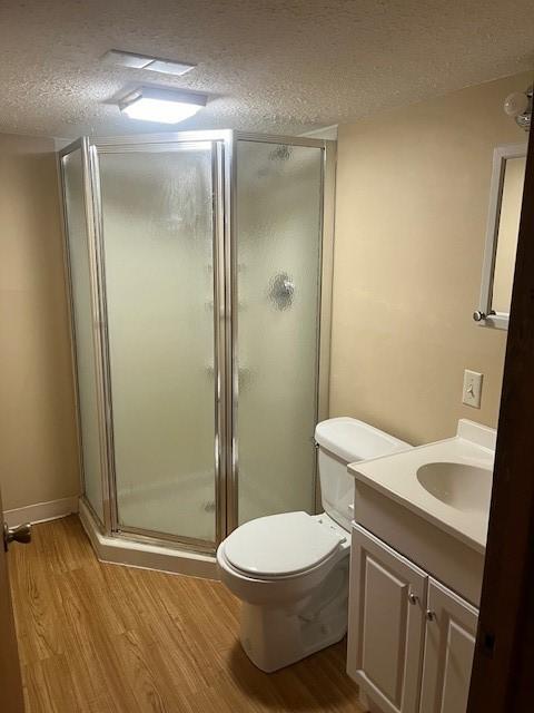 bathroom with vanity, hardwood / wood-style flooring, toilet, a textured ceiling, and a shower with shower door