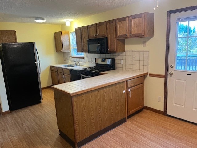 kitchen featuring sink, backsplash, tile countertops, black appliances, and light wood-type flooring