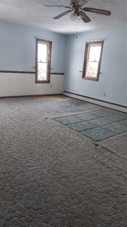 carpeted empty room featuring ceiling fan, baseboard heating, and a textured ceiling