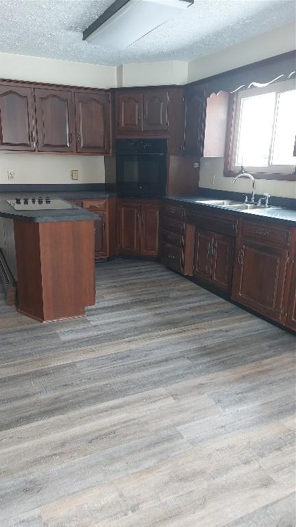 kitchen featuring dark countertops, a textured ceiling, light wood-type flooring, a sink, and black oven