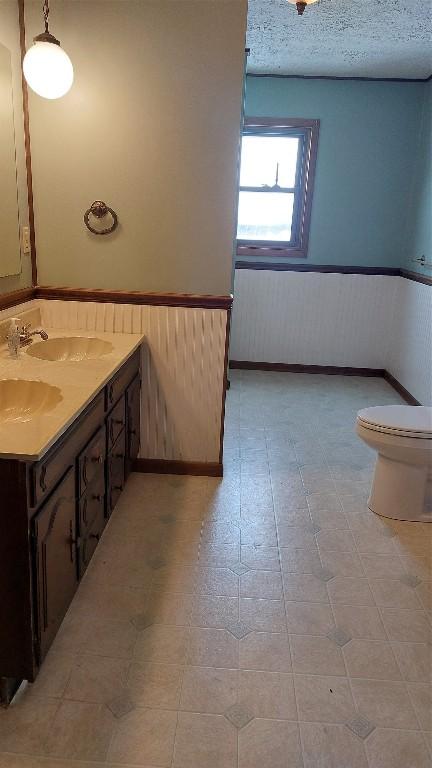 bathroom featuring a textured ceiling, wainscoting, vanity, and toilet