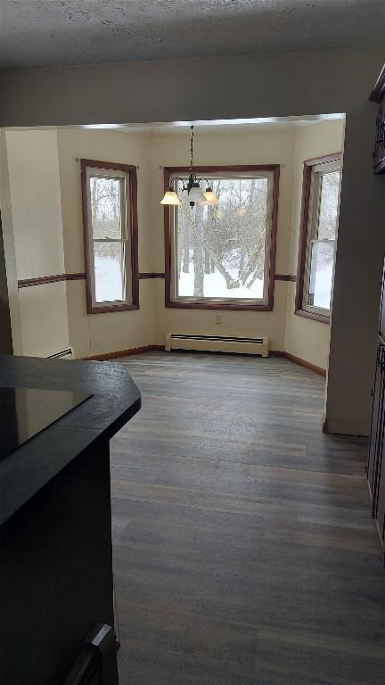 unfurnished dining area featuring an inviting chandelier, dark wood-type flooring, a textured ceiling, and a baseboard heating unit