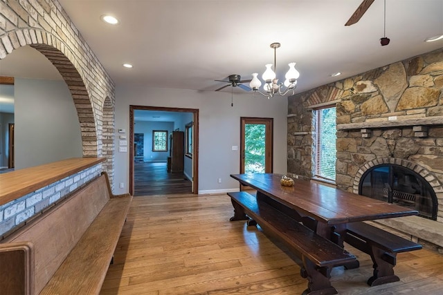 dining room featuring ceiling fan with notable chandelier, a stone fireplace, and light hardwood / wood-style flooring