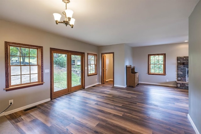 unfurnished living room featuring dark hardwood / wood-style floors, a stone fireplace, a wealth of natural light, and an inviting chandelier