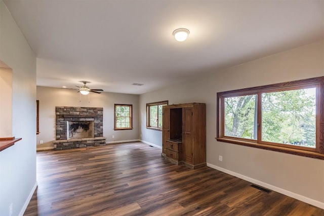 unfurnished living room featuring a stone fireplace, ceiling fan, and dark hardwood / wood-style floors