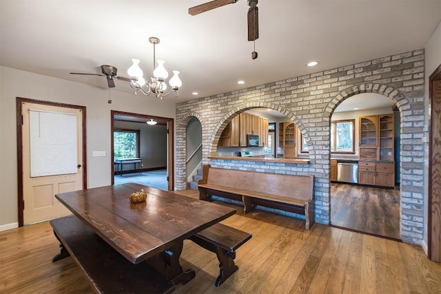 dining area featuring brick wall, ceiling fan with notable chandelier, and hardwood / wood-style flooring