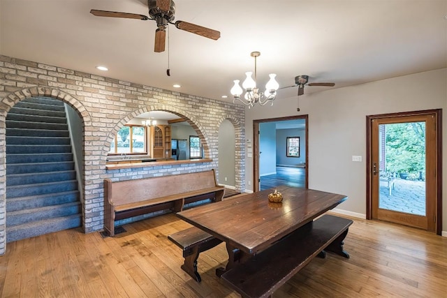 dining area featuring ceiling fan with notable chandelier, brick wall, and light hardwood / wood-style flooring