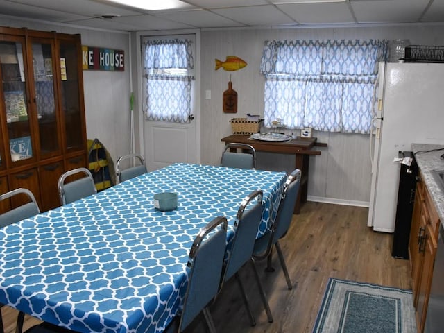 dining room with a paneled ceiling, wood walls, and wood-type flooring