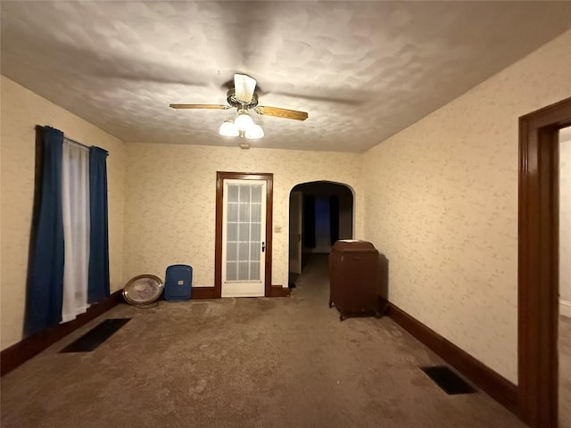 carpeted spare room featuring arched walkways, ceiling fan, visible vents, and baseboards