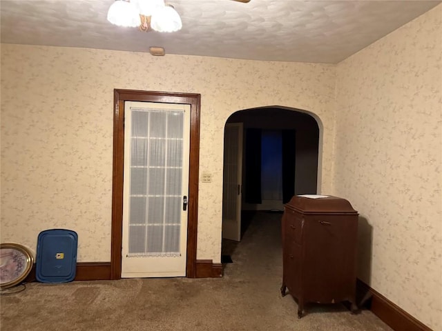 spare room featuring wallpapered walls, carpet, arched walkways, and baseboards