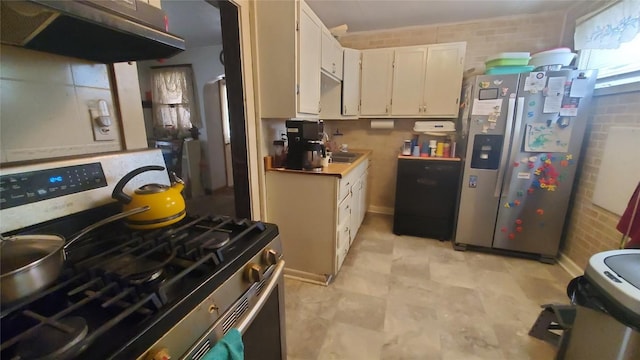 kitchen featuring white cabinets, appliances with stainless steel finishes, brick wall, and range hood