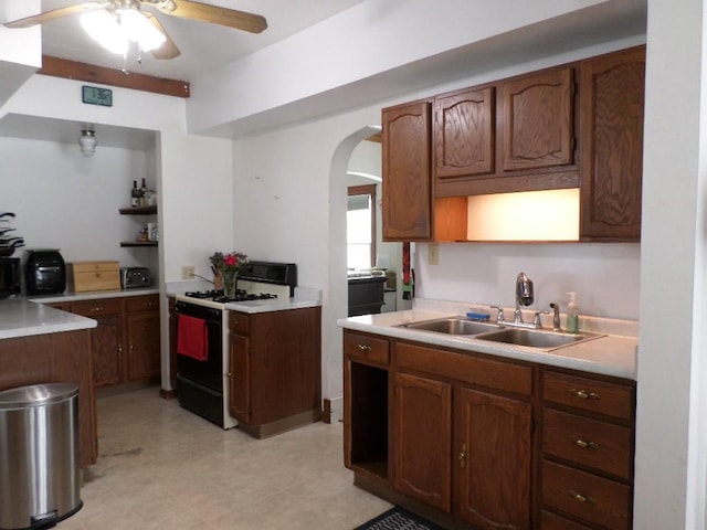 kitchen featuring arched walkways, range with gas cooktop, light countertops, a sink, and ceiling fan