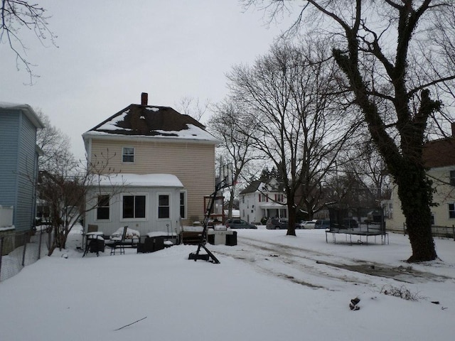 snow covered back of property with a trampoline and a chimney