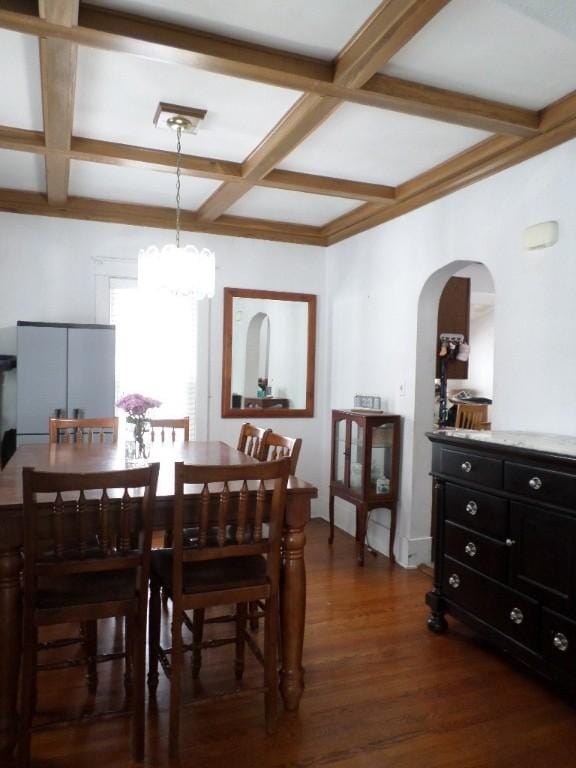 dining space featuring dark wood-style floors, arched walkways, coffered ceiling, and an inviting chandelier