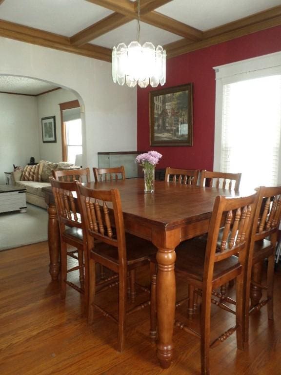 dining area with arched walkways, coffered ceiling, wood finished floors, and an inviting chandelier