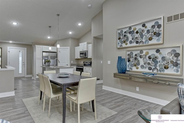 dining room featuring high vaulted ceiling, sink, and light wood-type flooring