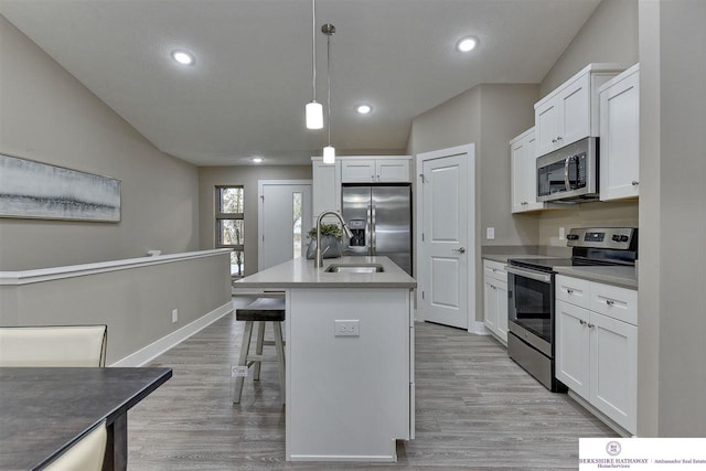 kitchen featuring hanging light fixtures, white cabinets, appliances with stainless steel finishes, light hardwood / wood-style floors, and a center island with sink