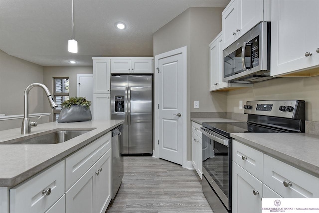 kitchen with white cabinets, decorative light fixtures, light hardwood / wood-style floors, and stainless steel appliances