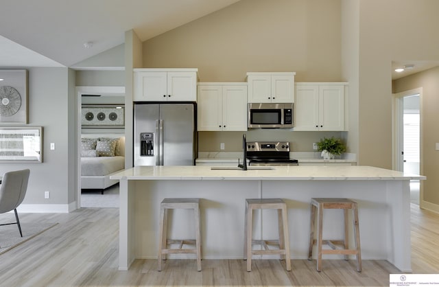 kitchen featuring light stone counters, stainless steel appliances, light hardwood / wood-style floors, white cabinetry, and high vaulted ceiling