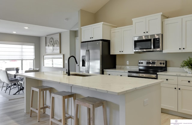 kitchen with appliances with stainless steel finishes, light hardwood / wood-style floors, white cabinetry, a kitchen island with sink, and vaulted ceiling