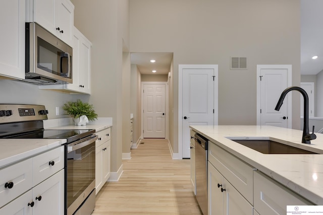 kitchen with light stone countertops, appliances with stainless steel finishes, light hardwood / wood-style floors, sink, and white cabinets