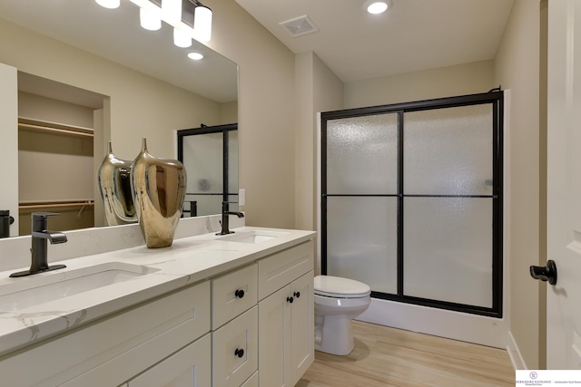 bathroom featuring a shower with shower door, wood-type flooring, dual sinks, toilet, and oversized vanity