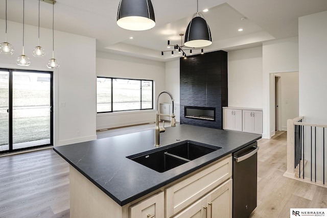 kitchen featuring an island with sink, a tray ceiling, light wood-type flooring, dishwasher, and sink