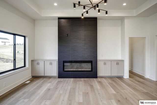 unfurnished living room featuring a tray ceiling, light hardwood / wood-style flooring, a chandelier, and a fireplace