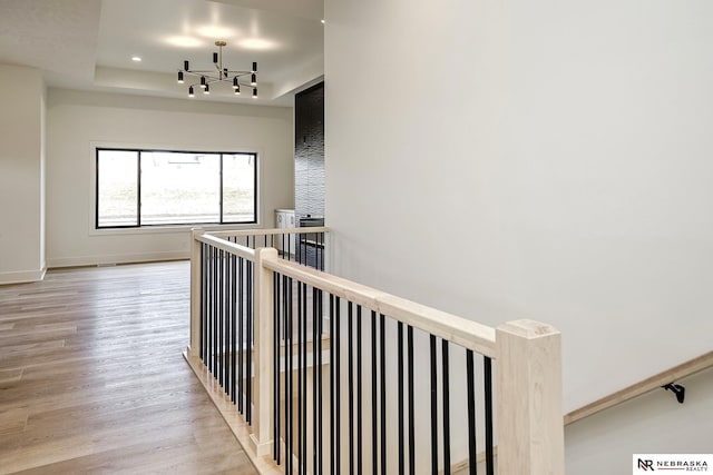 hallway with a raised ceiling, a chandelier, and light hardwood / wood-style flooring