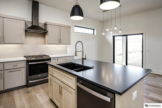 kitchen with stainless steel gas range oven, a kitchen island with sink, dishwasher, wall chimney range hood, and sink