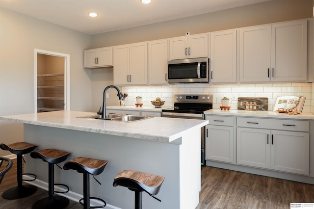 kitchen with backsplash, white cabinetry, dark hardwood / wood-style flooring, stainless steel appliances, and an island with sink