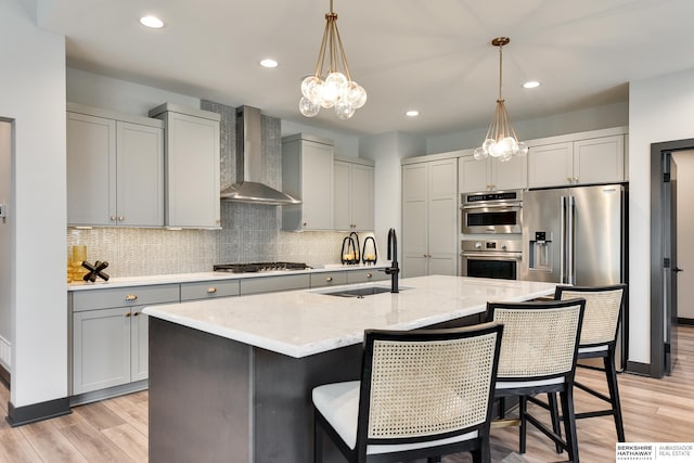 kitchen featuring wall chimney range hood, light hardwood / wood-style floors, stainless steel appliances, and a kitchen island with sink